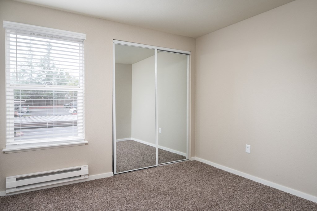 an empty bedroom with a window and a mirrored closet