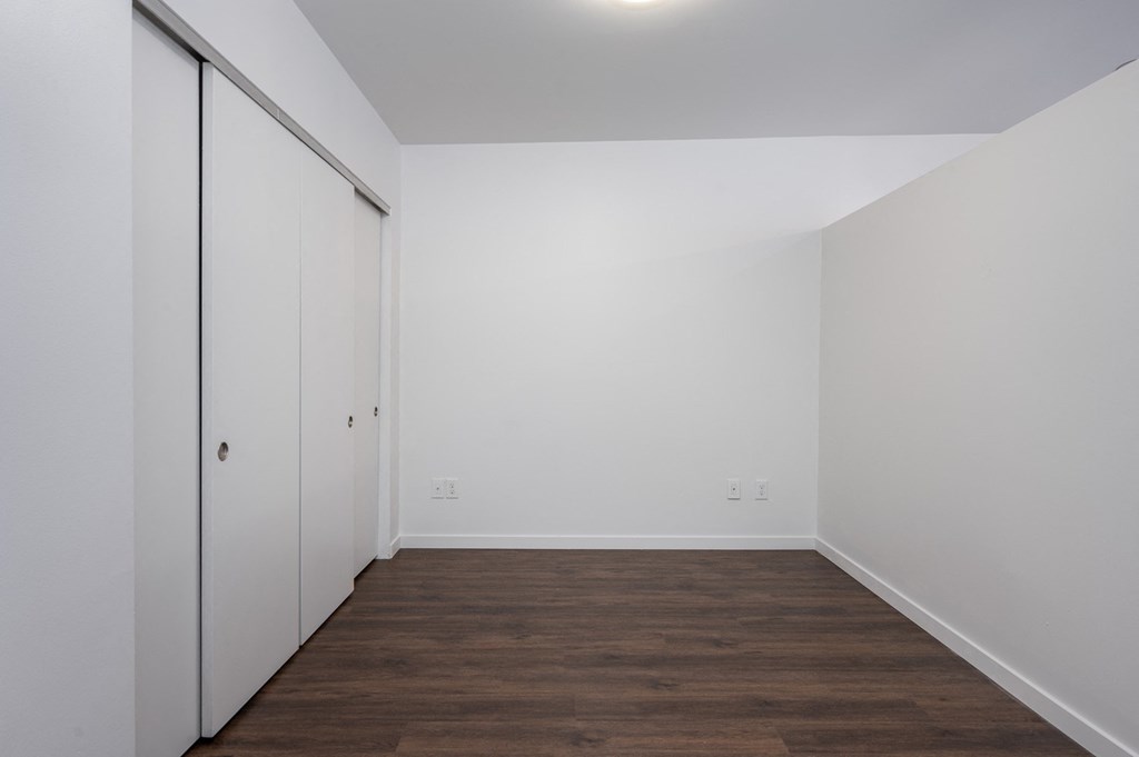 a bedroom with white walls and wood flooring and a closet