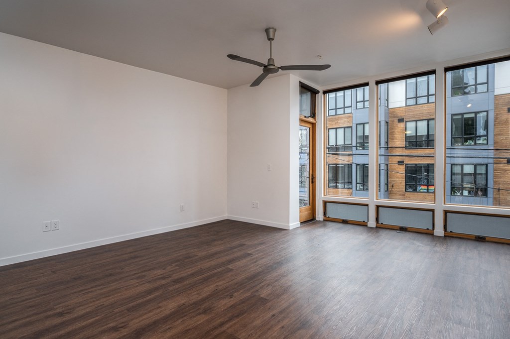 an empty living room with large windows and a ceiling fan