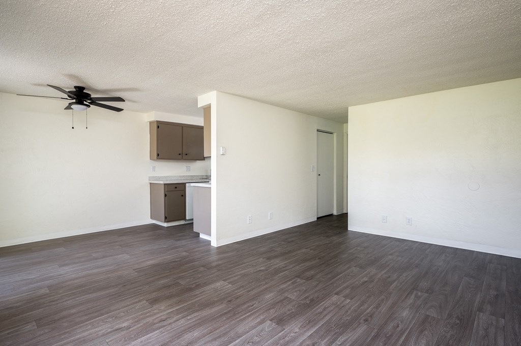an empty living room with a ceiling fan and a kitchen