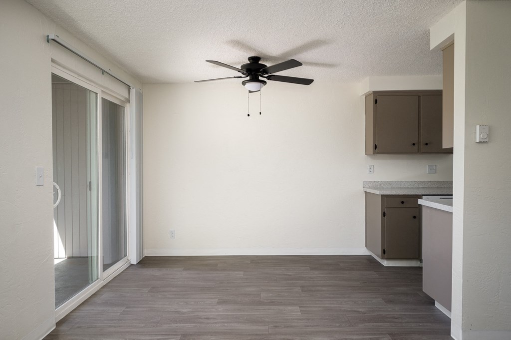 an empty living room with a ceiling fan and a kitchen
