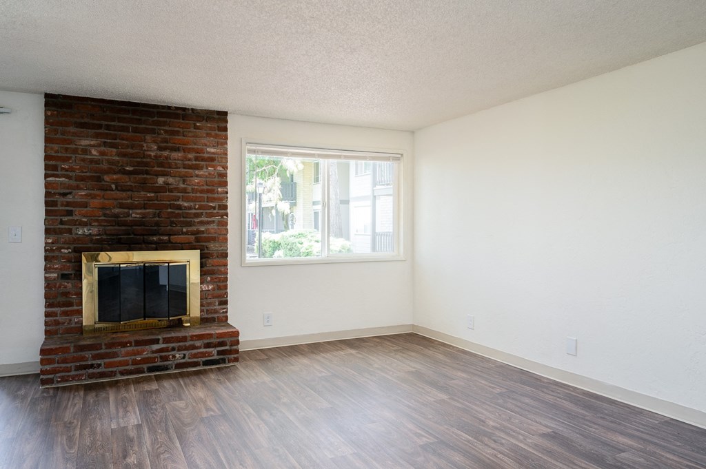 an empty living room with a brick fireplace and wooden floors