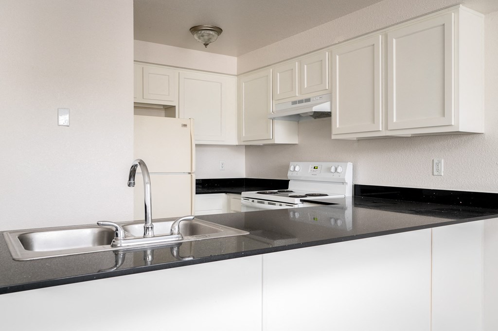 a kitchen with white cabinets and black counter tops and a sink