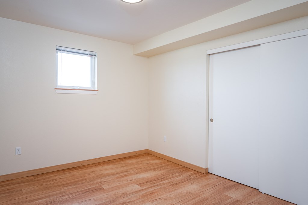 a bedroom with white walls and wood flooring and a window
