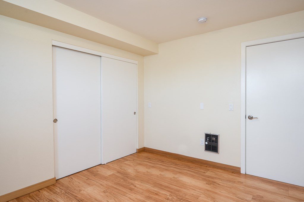 a bedroom with white walls and wood flooring and two closets