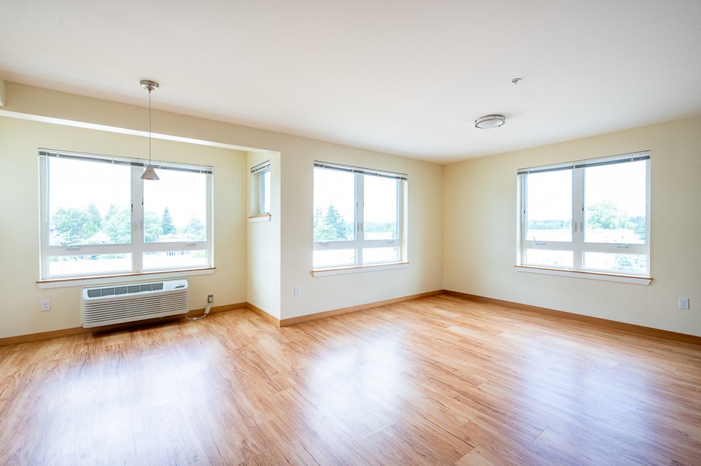 an empty living room with wood floors and three windows
