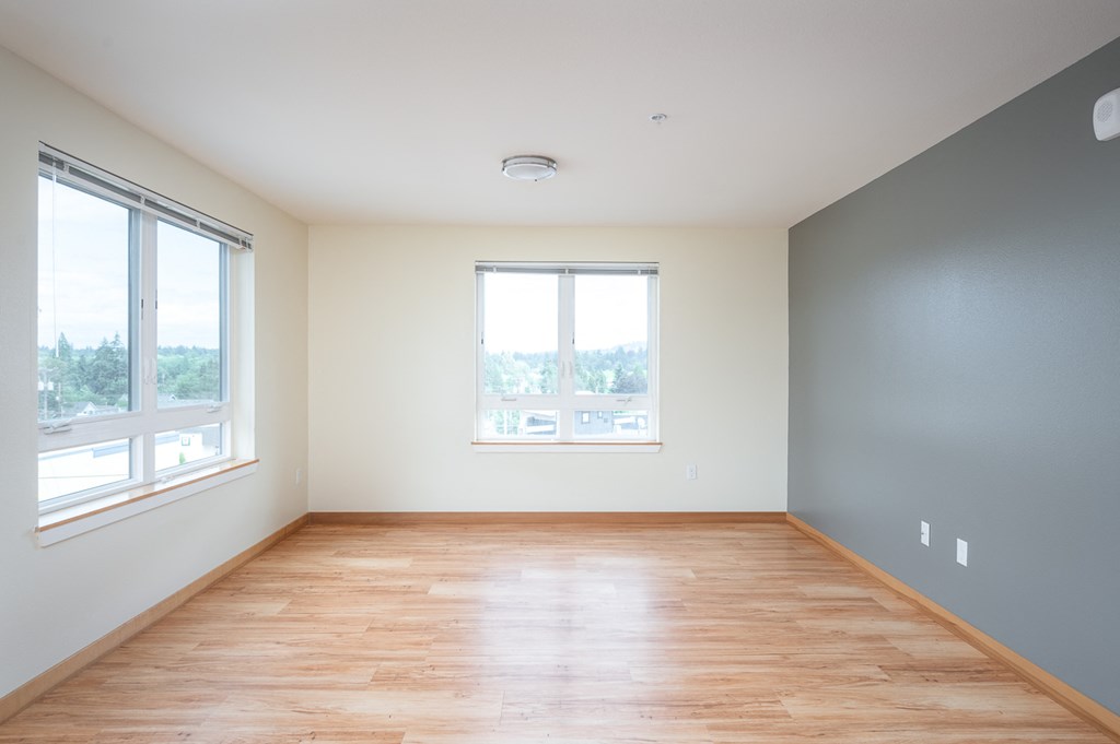 an empty room with wood floors and two windows