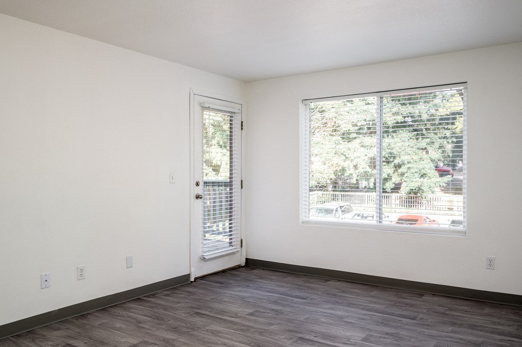 an empty living room with a large window and a door to a balcony