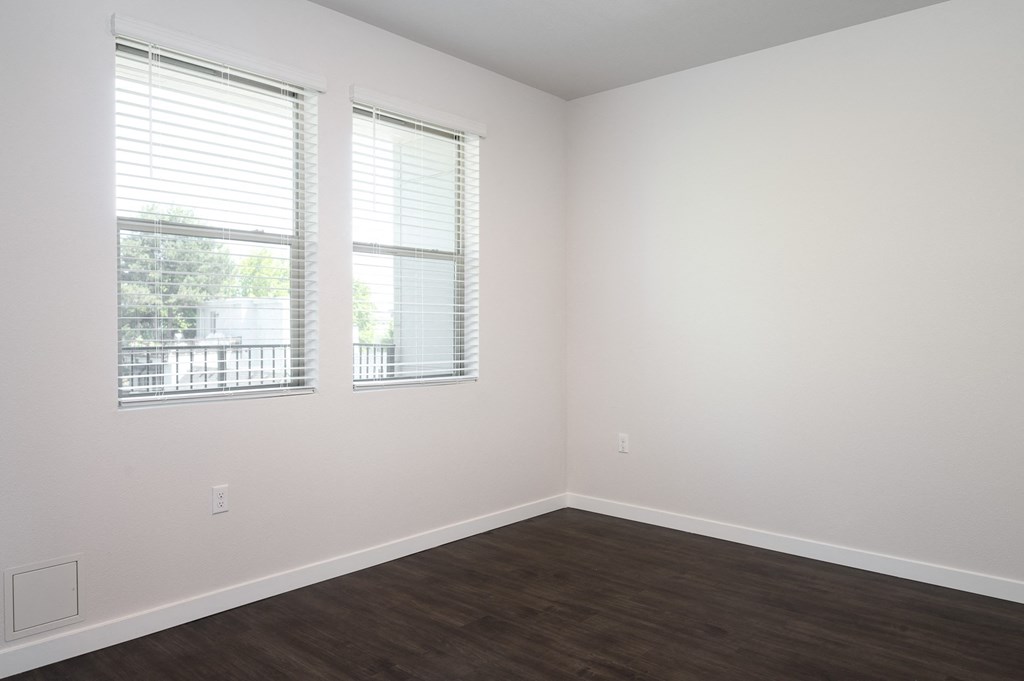 a bedroom with two windows and a hardwood floor