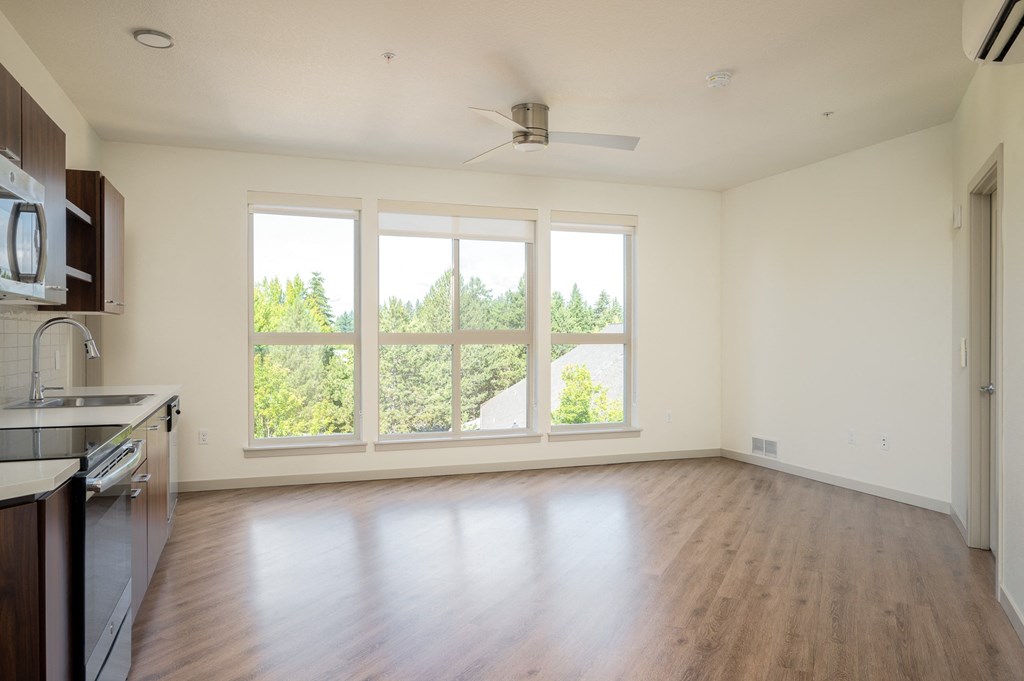 an empty living room with a large window and a kitchen