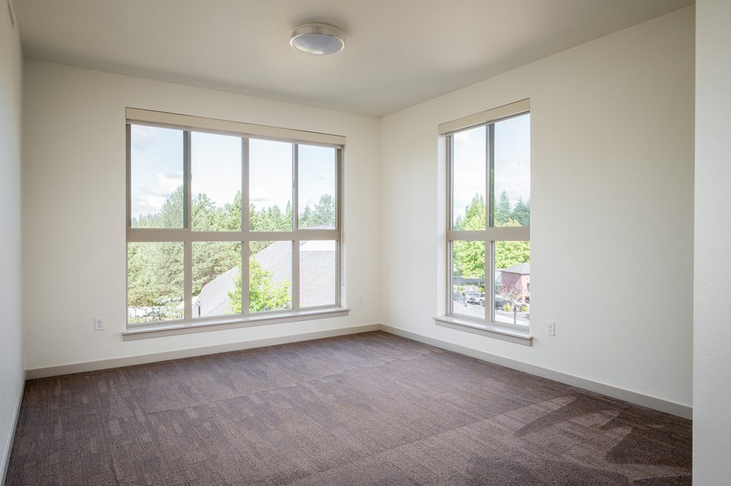 an empty living room with large windows and carpeting