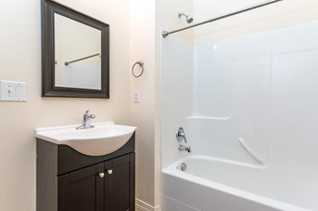 Bathroom with tub shower combination. Single vanity sink with cabinet below. Mirror above sink. - Photo Gallery 8