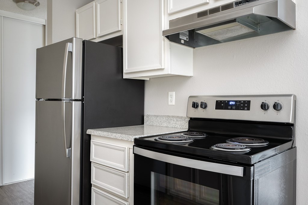 A black stove top oven with a digital display and a silver refrigerator in a kitchen.