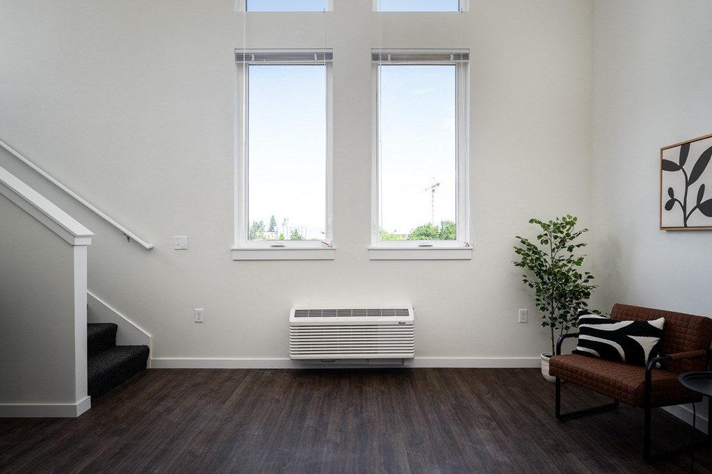 a living room with large windows, air conditioner, and stairs to loft space