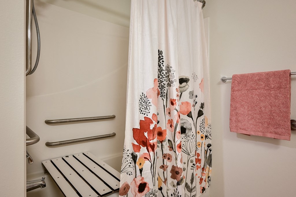 a shower with a floral shower curtain and a pink towel