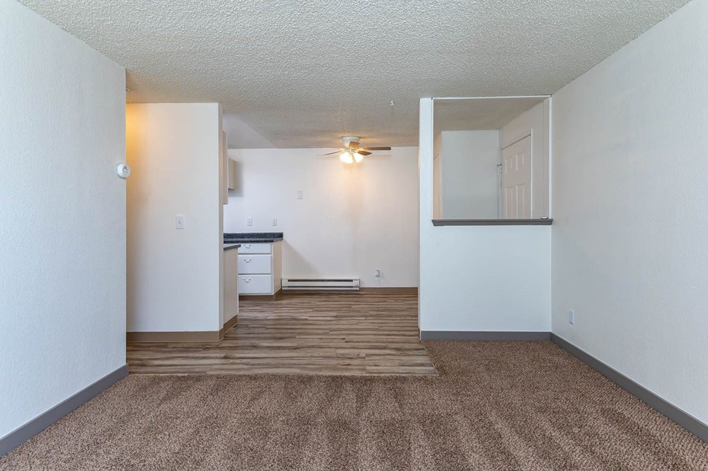 A room with a carpeted floor and a small kitchenette.