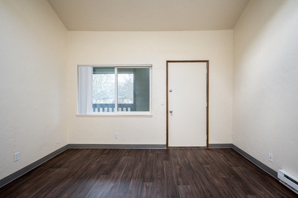 the bedroom of an empty apartment with wood flooring and a window