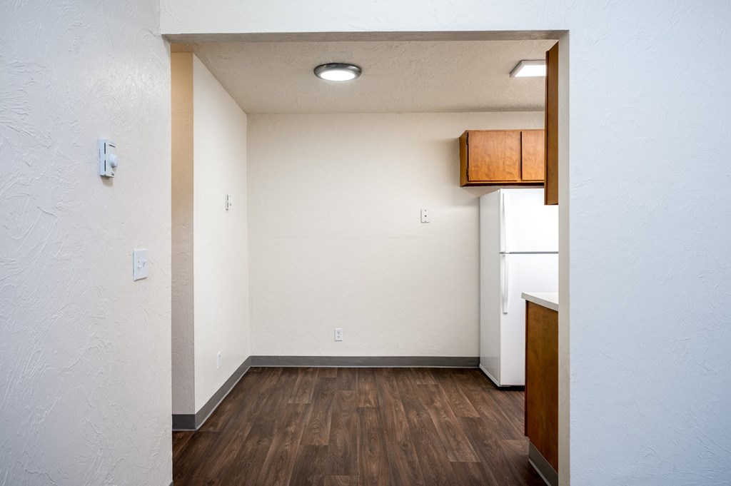 an empty kitchen with a refrigerator and wood floors