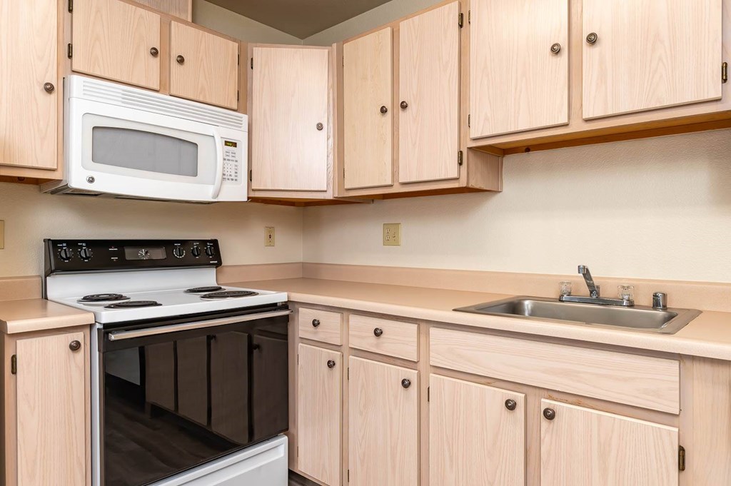 A kitchen with a white microwave oven mounted above a stove and wooden cabinets below.
