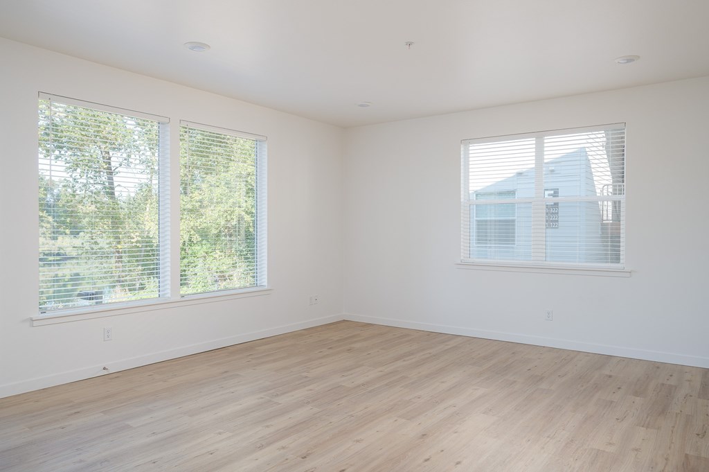 A room with wooden floors and two large windows.