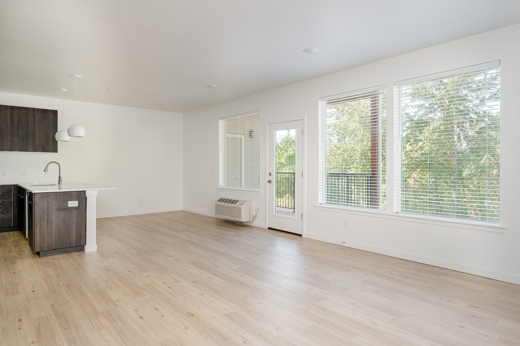 A room with wooden floors, white walls and large windows leading to a balcony..