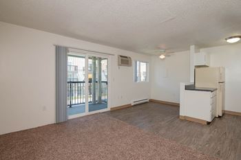 an empty living room with a refrigerator and a door to a balcony