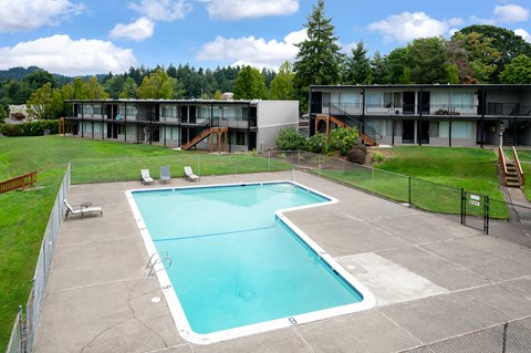 A large swimming pool in a fenced in area with a building in the background.
