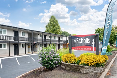 A sign for The Scholls apartment complex is in front of a building.