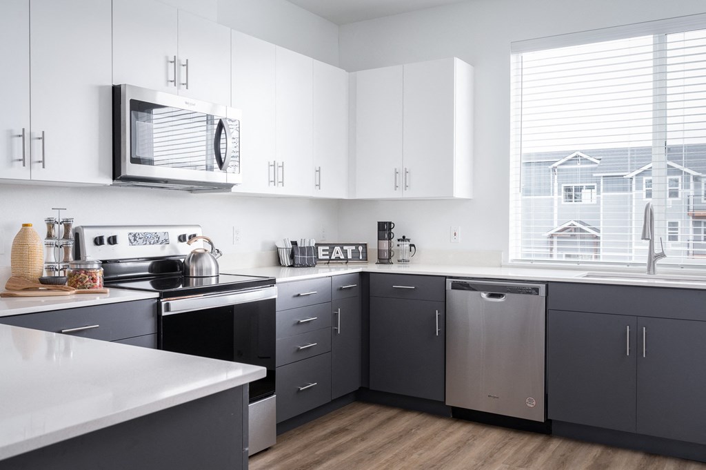 2 BR Apartments in Oregon City OR - Timberview Apartments and Townhomes - Bright Modern Kitchen with a Large Window, Stainless Steel Appliances, White Quartz Countertops, and White and Dark Grey Cabinetry