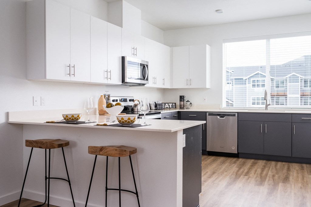 a kitchen with white cabinets, breakfast bar with two stools in front of it