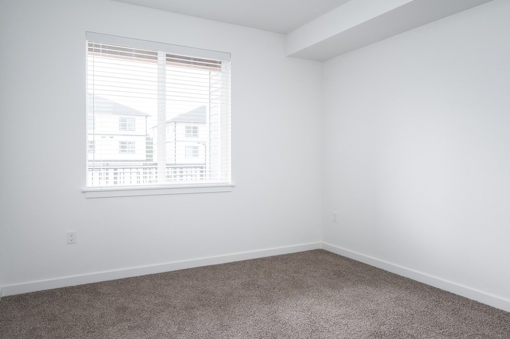 A room with a carpeted floor and a window showing a view of a house.