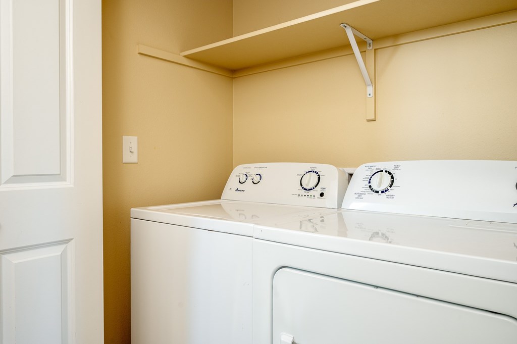 A white washing machine with a white door and a white shelf above it.