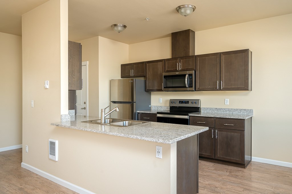 A kitchen with a granite counter top and brown cabinets.