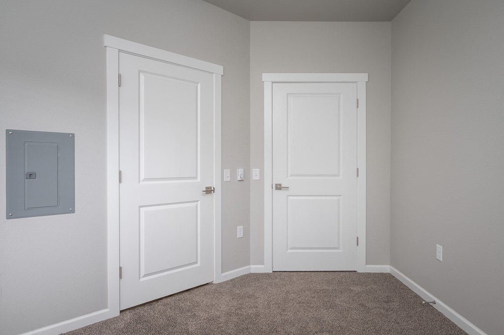 an empty bedroom with two doors and a carpeted floor