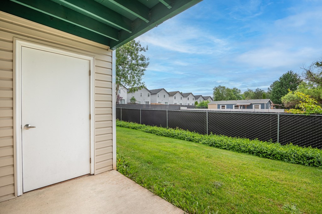 the private patio of a home with a white door and a fence