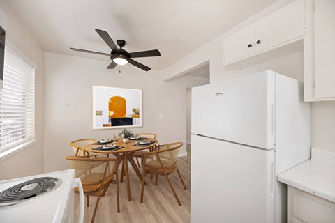 A white refrigerator sits next to a dining table in a kitchen.