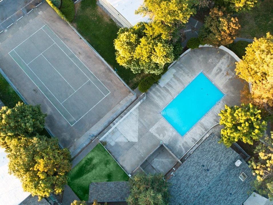 arial view of a tennis court and a pool in a backyard with trees