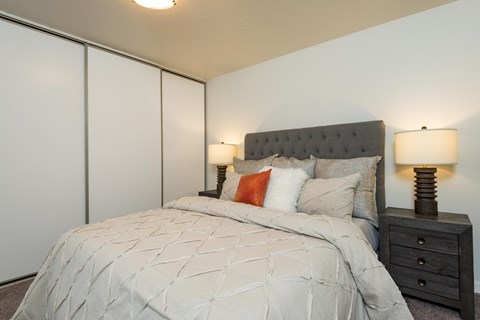 A bed with a grey headboard and a white comforter with a pattern on it.