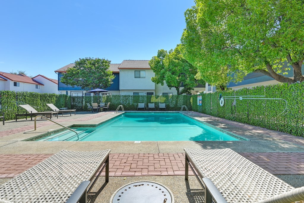 A pool surrounded by a brick patio and a metal fence.