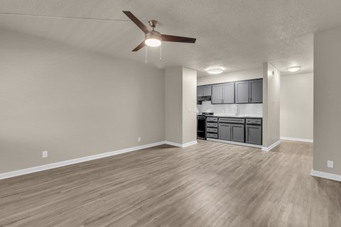 an empty living room with a ceiling fan and a kitchen