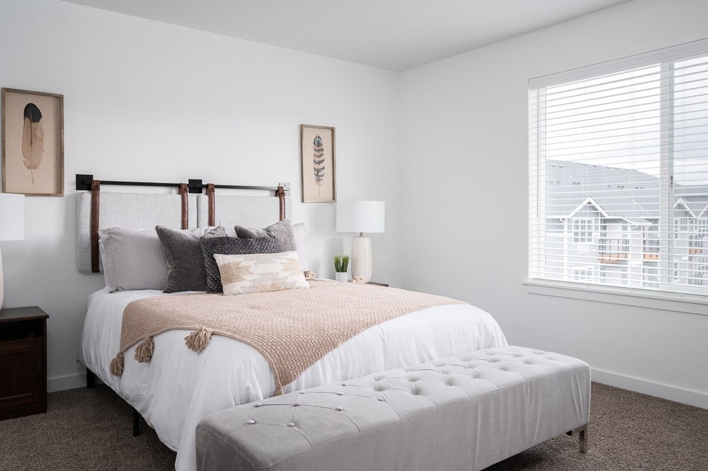 a bedroom with a bed and an ottoman in front of a window