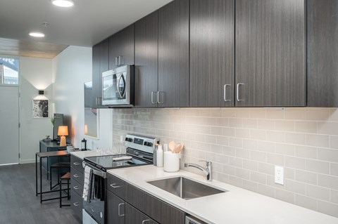 1 BR Apartments in Eugene OR - Crosswood Apartments - Modern Kitchen with Wood-Style Cabinetry, White Countertops, Stainless Steel Appliances, and a Small Dining Area