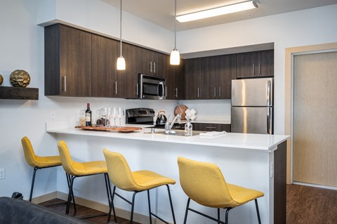 a kitchen with a counter with three yellow chairs