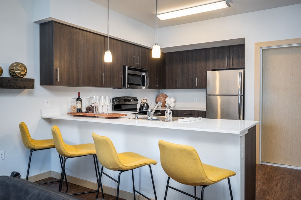 Dog-Friendly Apartments in Everett WA - The Waterline - Kitchen with Stainless Steel Appliances, Quartz Countertops, Dark Wood-Style Cabinetry, Pendant Lighting, Breakfast Bar, and Vinyl Hardwood Floo