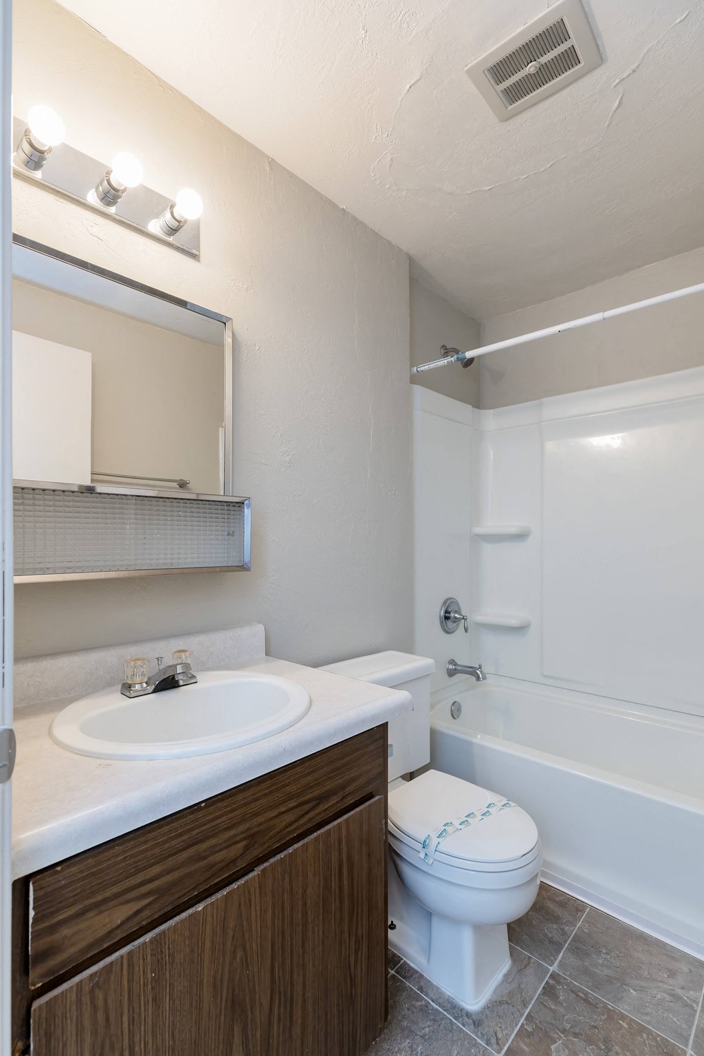 A white toilet with a brown cabinet and a white sink with a mirror above it.