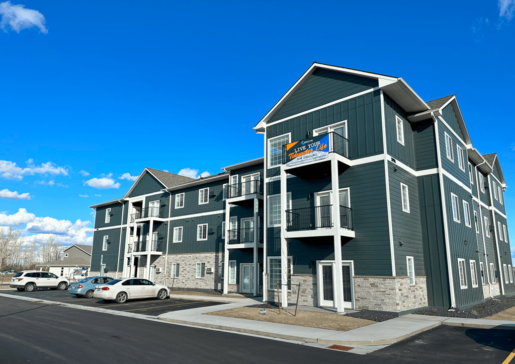 a green apartment building with cars parked outside