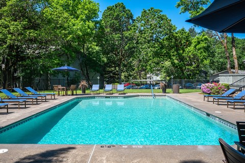 a swimming pool with chairs and umbrellas in a yard with trees