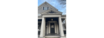 the front of the house has a large porch with columns and a window above the door