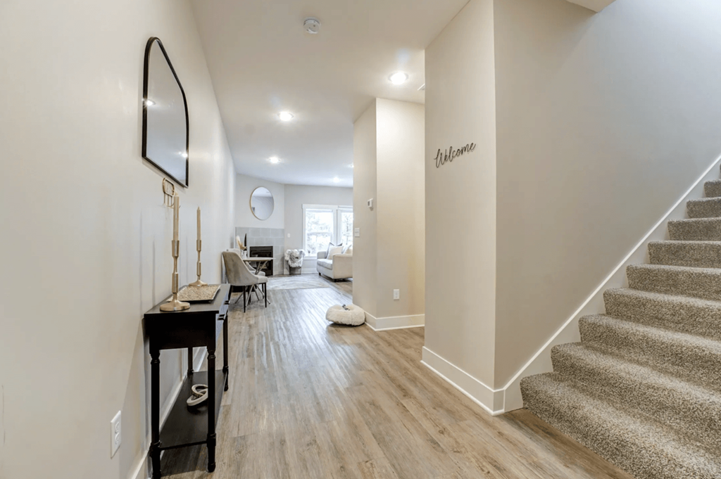 A hallway with a staircase and a mirror on the wall.