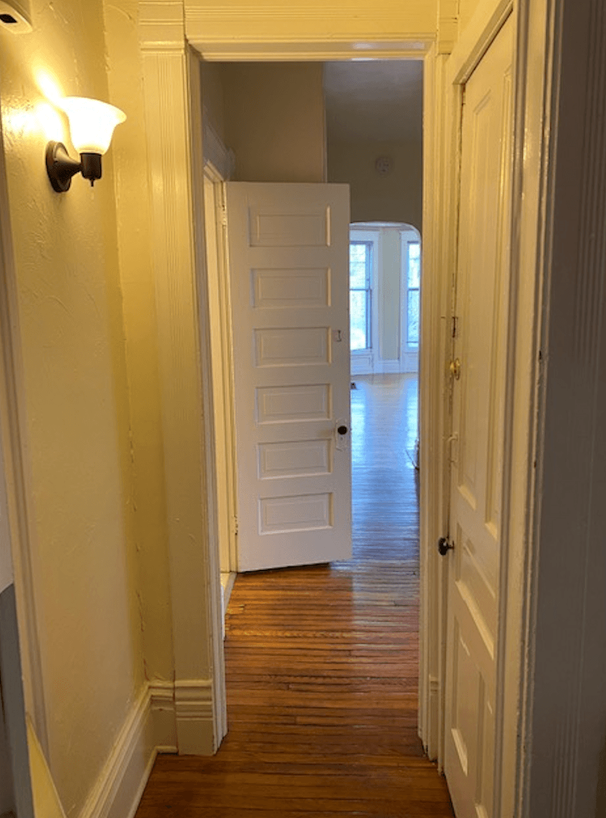a hallway with an open white door and a wooden floor